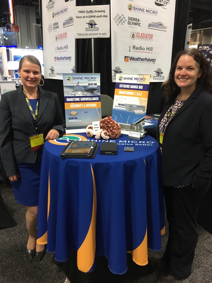 Shine Micro Marketing Manager Stephanie Nevarez and PNDC Puget Sound Regional Director Meghan Murphy stand at the Shine Micro table in the PNDC pavilion at AUSA in Washington, D.C.